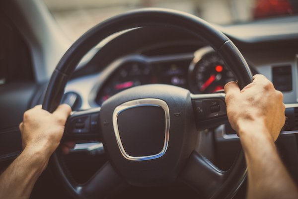 Close up shot of a man's hands holding a car's steering wheel.