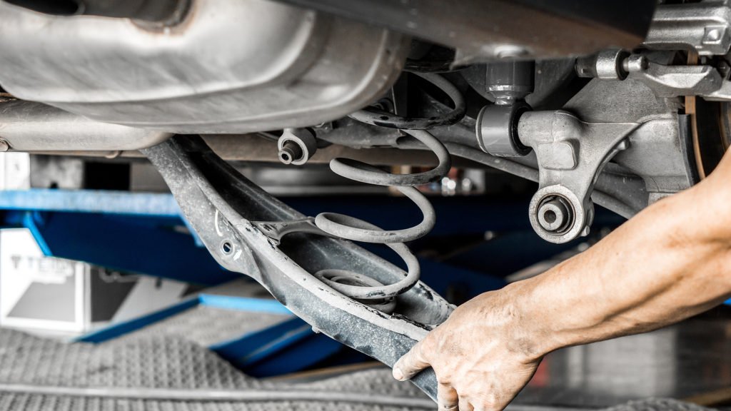 Car suspension and car mechanic service concept - Close up car suspension service with hand of mechanic man in maintenance car garage with flare light effect and copy space, use for car suspension service content